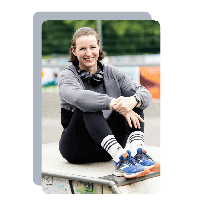 Ein Foto der Fitnesstrainerin Hanna Winter, die lachend in einem Skatepark auf einer Rampe sitzt.