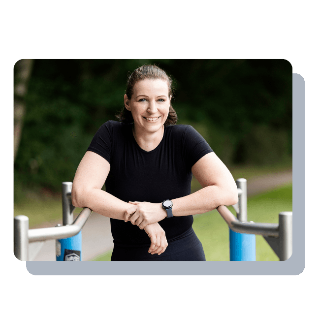 Ein Foto der Fitnesstrainerin Hanna Winter, die ihre angewinkelten Arme auf einem Gerüst abstützt und selbstbewusst in die Kamera lächelt.